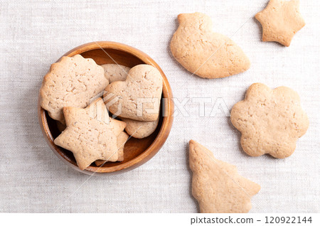 Homemade gingerbread cookies in a wooden bowl on linen fabric. Sweet, light brown and flat baked goods for Christmas season, flavored with ginger, cloves, nutmeg, cinnamon, and sweetened with honey. 120922144