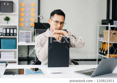 Asian man using laptop and tablet while sitting at her working place. Concentrated at work. Asian man using laptop and tablet while sitting at her working place. Concentrated at work. 120922853