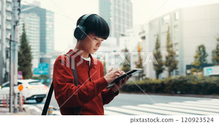 City, headphones and man in street with tablet, morning commute or online search on crosswalk. Urban travel, pedestrian crossing and Japanese university student on digital app for music streaming 120923524
