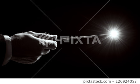 A hand holds a wand against a dark background, creating a bright light. Concept of magic and mystery. For fantasy and magical themed content. 120924052