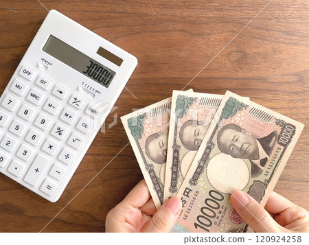 A woman's hand holding 30,000 yen and a calculator on a desk 120924258