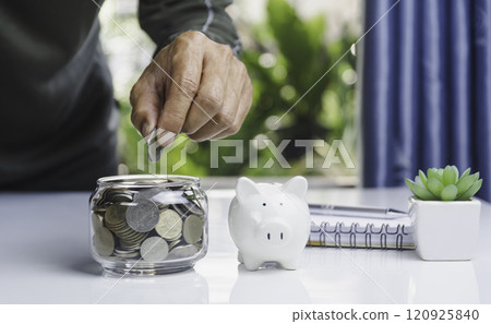 Hand with money coins in clear glass, Business investment growth concept, saving concept, Hand putting coin in clear jar. 120925840