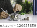 Hand with money coins in clear glass, Business investment growth concept, saving concept, Hand putting coin in clear jar. 120925859