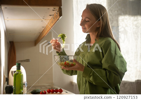 Woman prepares a colorful salad in a bright kitchen while smiling and enjoying a healthy cooking moment 120927153