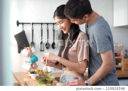 Happy cheerful Asian young couple preparing a vegetable salad in kitchen together in weekend, man holding lovely cute Maltese dog to see his girlfriend making a salad in kitchen. Happy cheerful Asian young couple preparing a vegetable salad in kitchen together in weekend, man holding lovely cute Maltese dog to see his girlfriend making a salad in kitchen. 120928596