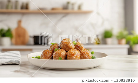 Homemade pork meatballs glazed in a savory sauce, garnished with fresh green onions, served on white plate in modern kitchen setting, evoking comfort food and culinary delight 120928910