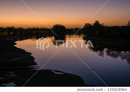 The River Thames reflecting the pre-dawn glow and a streetscape lined with winter trees and street lamps in Kew Bridge, a suburb of London 120928964