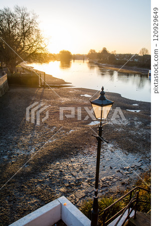 The River Thames illuminated by the rising sun and the riverbed exposed by the low tide, Kew Bridge, on the outskirts of London 120929649