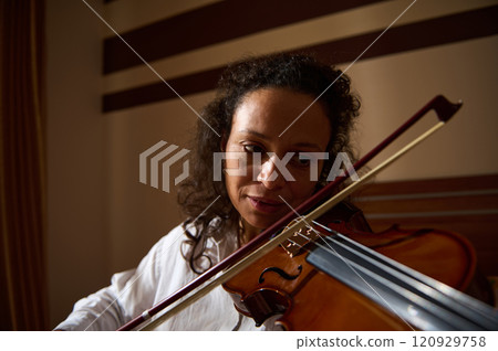 Young woman playing the violin with passion in a dimly lit room 120929758