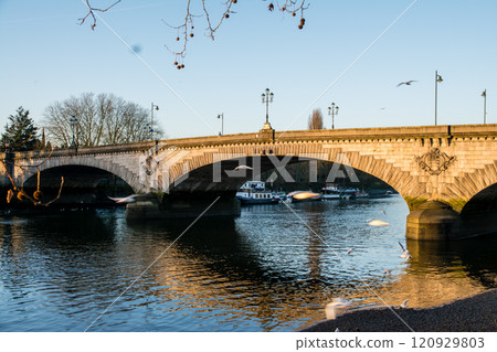 Kew Bridge, a historic stone arch structure spanning the River Thames bathed in the orange sunlight of early morning Kew Bridge, a historic stone arch structure spanning the River Thames bathed in the orange sunlight of early morning 120929803