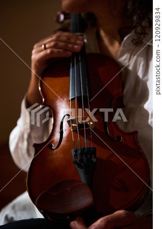 Close-up of a musician gently holding a classical violin in warm light Close-up of a musician gently holding a classical violin in warm light 120929834