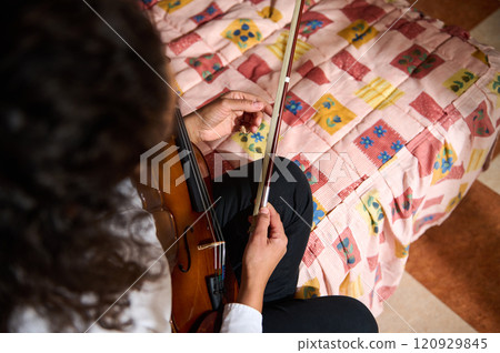 Close-up of a person tuning a violin on a colorful bedspread 120929845