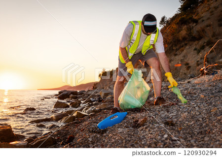 Man volunteer wearing vest and rubber gloves picking up garbage on beach. Copy space. Concept of Earth Day and environmental disaster Man volunteer wearing vest and rubber gloves picking up garbage on beach. Copy space. Concept of Earth Day and environmental disaster 120930294