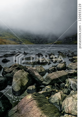 A view of a lake surrounded by rugged hills, with a thick fog obscuring the distant peaks. A view of a lake surrounded by rugged hills, with a thick fog obscuring the distant peaks. 120933119