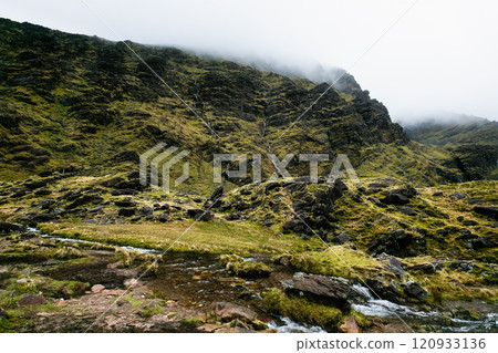 Majestic hillside with flowing water and mist in the landscape during a cloudy day in nature scenery. Majestic hillside with flowing water and mist in the landscape during a cloudy day in nature scenery. 120933136