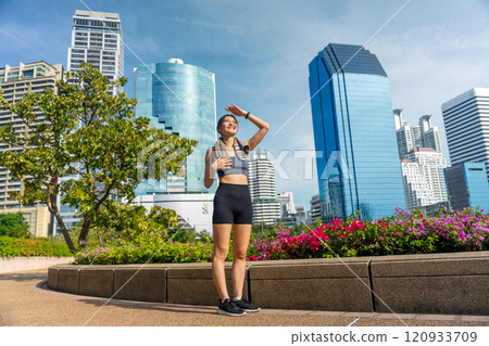 Asian sport woman stand to relax after exercise in public garden with high building of big city in background and soft light. Asian sport woman stand to relax after exercise in public garden with high building of big city in background and soft light. 120933709