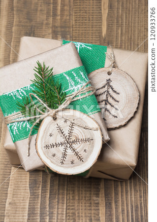 Christmas gift box in rustic style wrapped in craft paper with decor of wooden sliced with woodburning symbol. 120933766