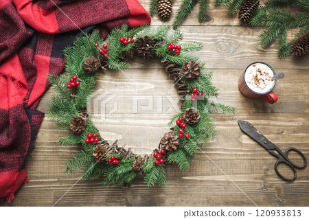 Christmas composition of wreath, checkered pleid, cup of coffee on wooden board. Flat lay. Top view. Copy space. Xmas card 120933813