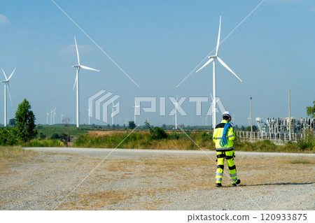 Back of wind turbine or windmill worker carry the rope walk during work in workplace field in day time and wind turbine are in the background. 120933875