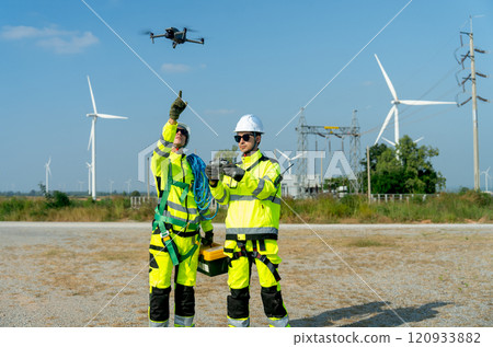 Wind turbine or windmill workers use drone to work in workplace field during day time with one point to the drone and wind turbine are in the background. Wind turbine or windmill workers use drone to work in workplace field during day time with one point to the drone and wind turbine are in the background. 120933882