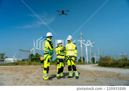 Wide shot of wind turbine or windmill worker woman or engineer use controller to control the drone to work with her co-worker team in workplace field. 120933886
