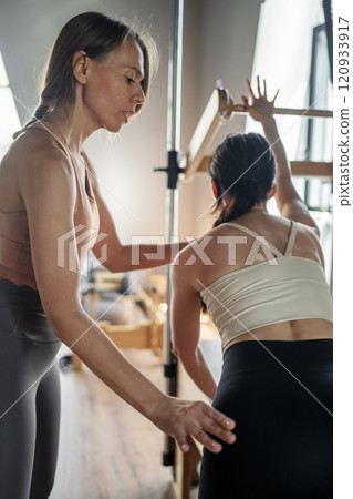 Woman doing Swan exercise on Pilates Reformer for the chest and back muscles, focusing on flexibility, strength, and control with determination 120933917