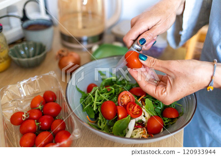 Women's hands slice cherry tomatoes for a salad and place them in a bowl with arugula and shredded cabbage. Women's hands slice cherry tomatoes for a salad and place them in a bowl with arugula and shredded cabbage. 120933944