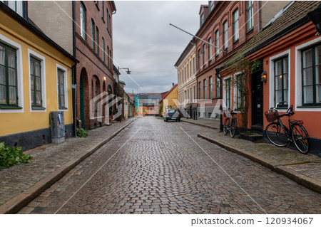 An empty narrow cobblestone street with old colorful buildings with brick walls, Lund, Sweden 120934067