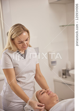lifting massage, aesthetic salon, beauty spa. Beautiful female has facial massage in beauty clinic, young woman's face lying on back, getting face lifting massage in beauty spa concept, towel on head lifting massage, aesthetic salon, beauty spa. Beautiful female has facial massage in beauty clinic, young woman's face lying on back, getting face lifting massage in beauty spa concept, towel on head 120934906