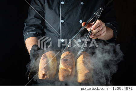 In a warm kitchen filled with steam, a chef uses tongs to lift golden-brown loaves from a baking tray, showcasing the art of bread-making and culinary expertise in action In a warm kitchen filled with steam, a chef uses tongs to lift golden-brown loaves from a baking tray, showcasing the art of bread-making and culinary expertise in action 120934971