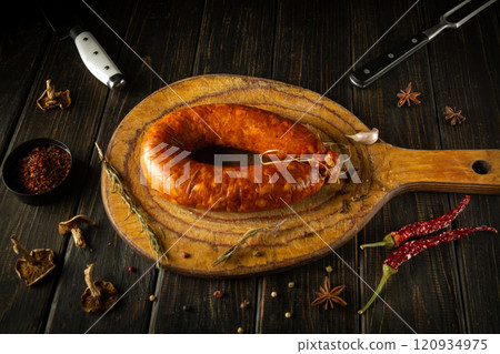 A beautifully crafted sausage rests on a rustic cutting board, surrounded by vibrant spices and herbs. The warm tones create an inviting atmosphere in this cozy kitchen setting A beautifully crafted sausage rests on a rustic cutting board, surrounded by vibrant spices and herbs. The warm tones create an inviting atmosphere in this cozy kitchen setting 120934975