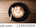 Artistic latte with foam design served in a black cup on table 120935900