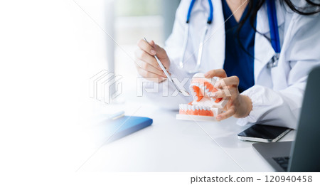 Concentrated dentist sitting at table with jaw samples tooth model and working with tablet and laptop in dental office Concentrated dentist sitting at table with jaw samples tooth model and working with tablet and laptop in dental office 120940458