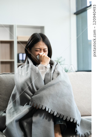 Young Asian woman suffering from flu symptoms, covered with a blanket on a sofa. Concept of illness, healthcare, and recovery 120940493