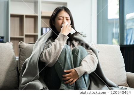 Young Asian woman suffering from flu symptoms, covered with a blanket on a sofa. Concept of illness, healthcare, and recovery 120940494