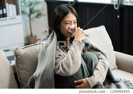 Young Asian woman suffering from flu symptoms, covered with a blanket on a sofa. Concept of illness, healthcare, and recovery 120940495