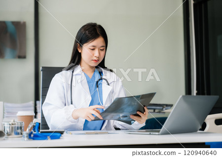Confident young female doctor in white medical uniform sit at desk working on computer. Smiling use laptop Confident young female doctor in white medical uniform sit at desk working on computer. Smiling use laptop 120940640