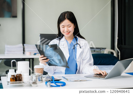 Confident young female doctor in white medical uniform sit at desk working on computer. Smiling use laptop Confident young female doctor in white medical uniform sit at desk working on computer. Smiling use laptop 120940641
