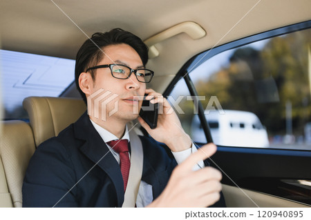 Businessman sitting in the back seat talking on a smartphone 120940895