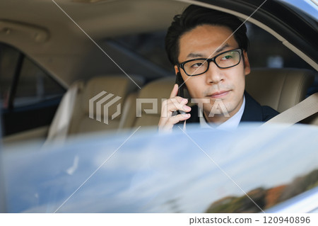 Businessman sitting in the back seat talking on a smartphone 120940896