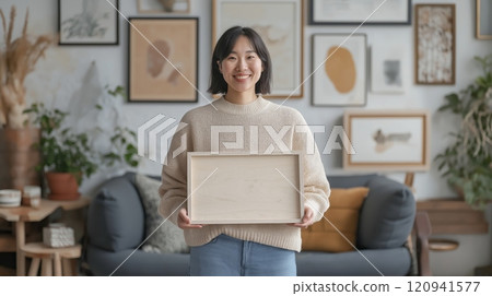 Cheerful east asian woman holding wooden tray in art-filled living room 120941577