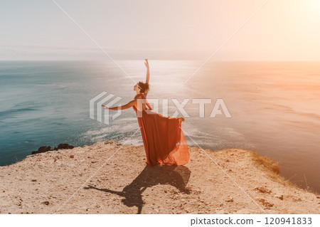 Woman red dress sea. Female dancer in a long red dress posing on a beach with rocks on sunny day. Girl on the nature on blue sky background. 120941833