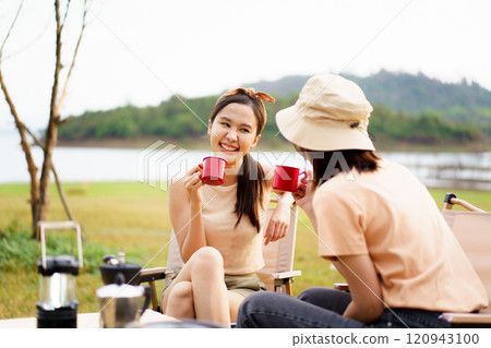Happy cheerful Asian young women - friends camping in the lake forest and enjoy drinking a cup of tea or coffee. Female friends on a camping trip in the natural park in summer. Happy cheerful Asian young women - friends camping in the lake forest and enjoy drinking a cup of tea or coffee. Female friends on a camping trip in the natural park in summer. 120943100