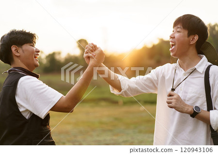 Happy Asian men looking at the beautiful sunlight during the sunset behind mountain together. Friends touch - hold hands together. Happy Asian men looking at the beautiful sunlight during the sunset behind mountain together. Friends touch - hold hands together. 120943106