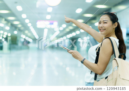 Beautiful happy Asian backpacker passenger holding a passport and mobile phone on hand while walking at the airport terminal. Woman looking at smartphone screen to check a message. Beautiful happy Asian backpacker passenger holding a passport and mobile phone on hand while walking at the airport terminal. Woman looking at smartphone screen to check a message. 120943185