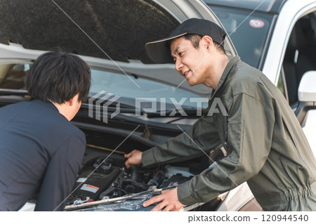 A male mechanic explaining something to a driver in the engine room of a car A male mechanic explaining something to a driver in the engine room of a car 120944540