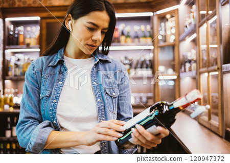 A woman is looking at a bottle of wine in a store 120947372