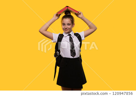 Teen girl holding book over head, wearing school uniform 120947856