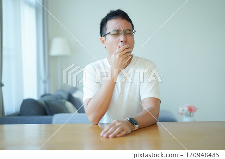 Asian man with an glasses in white t-shirt is relaxing in living room at home. A lonely man in white t-shirt portrait. 120948485