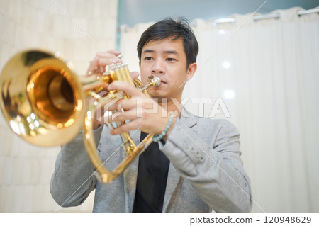 Asian man plays cornet. A solo Asian skillful musician is playing or practicing cornet in the restaurant. A man enjoy playing cornet or trumpet. 120948629